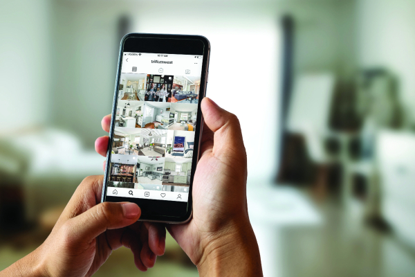 a person holding a cell phone, looking at the TrilliumWest Instagram page which shows real estate listings
