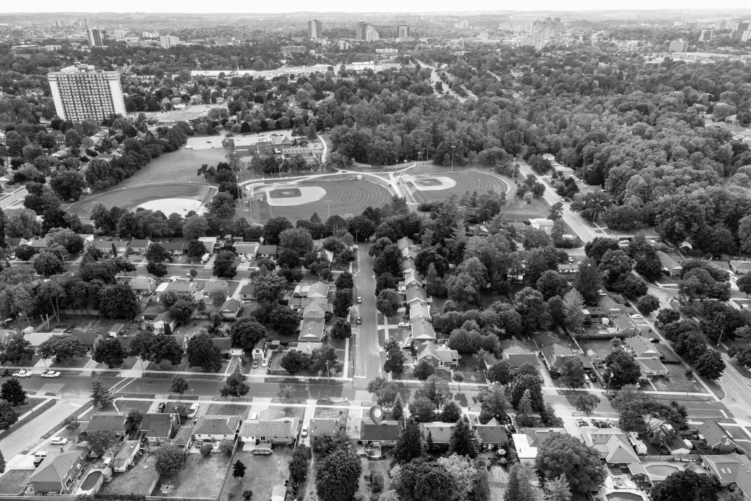 a drone photo looking over the Breithaupt Park neighbourhood in East Kitchener. streets lined with homes and trees, baseball diamonds at breithaupt park, apartment buildings and a forest area
