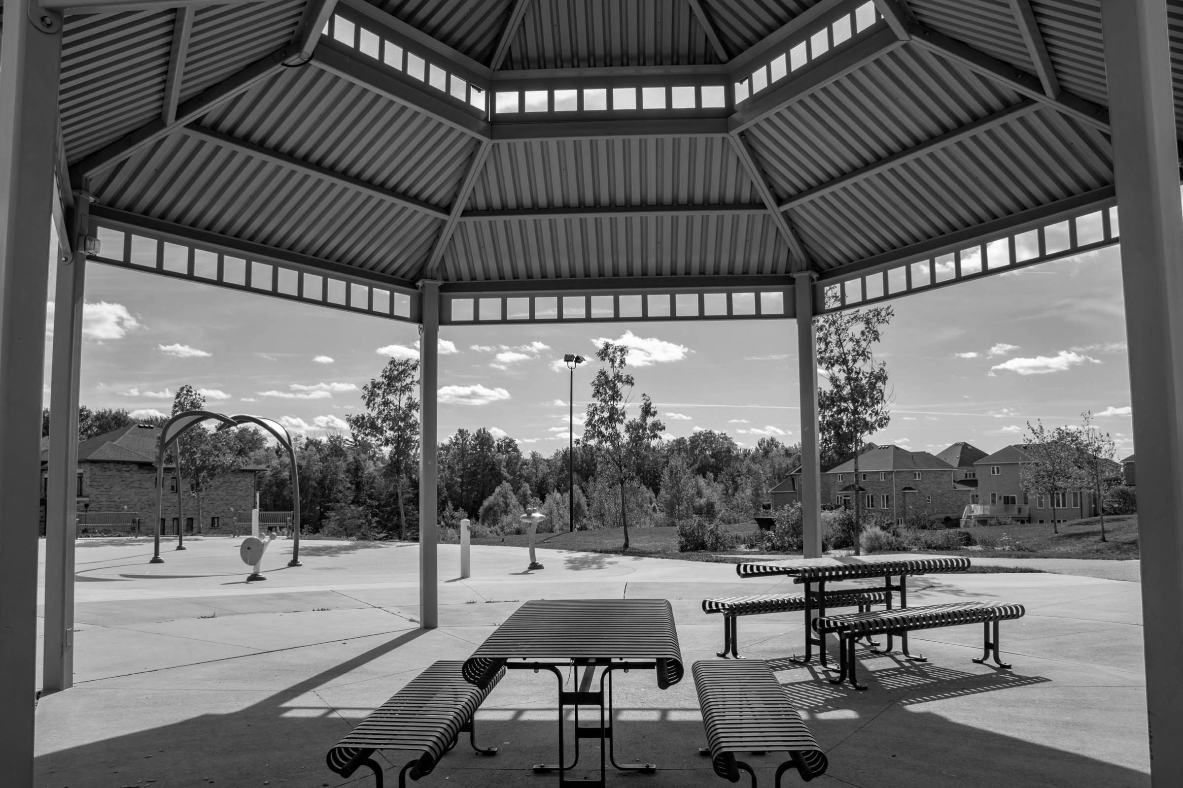A picnic table underneath a gazebo at a park in Kortright East, Guelph. There is a slashpad and houses in the background