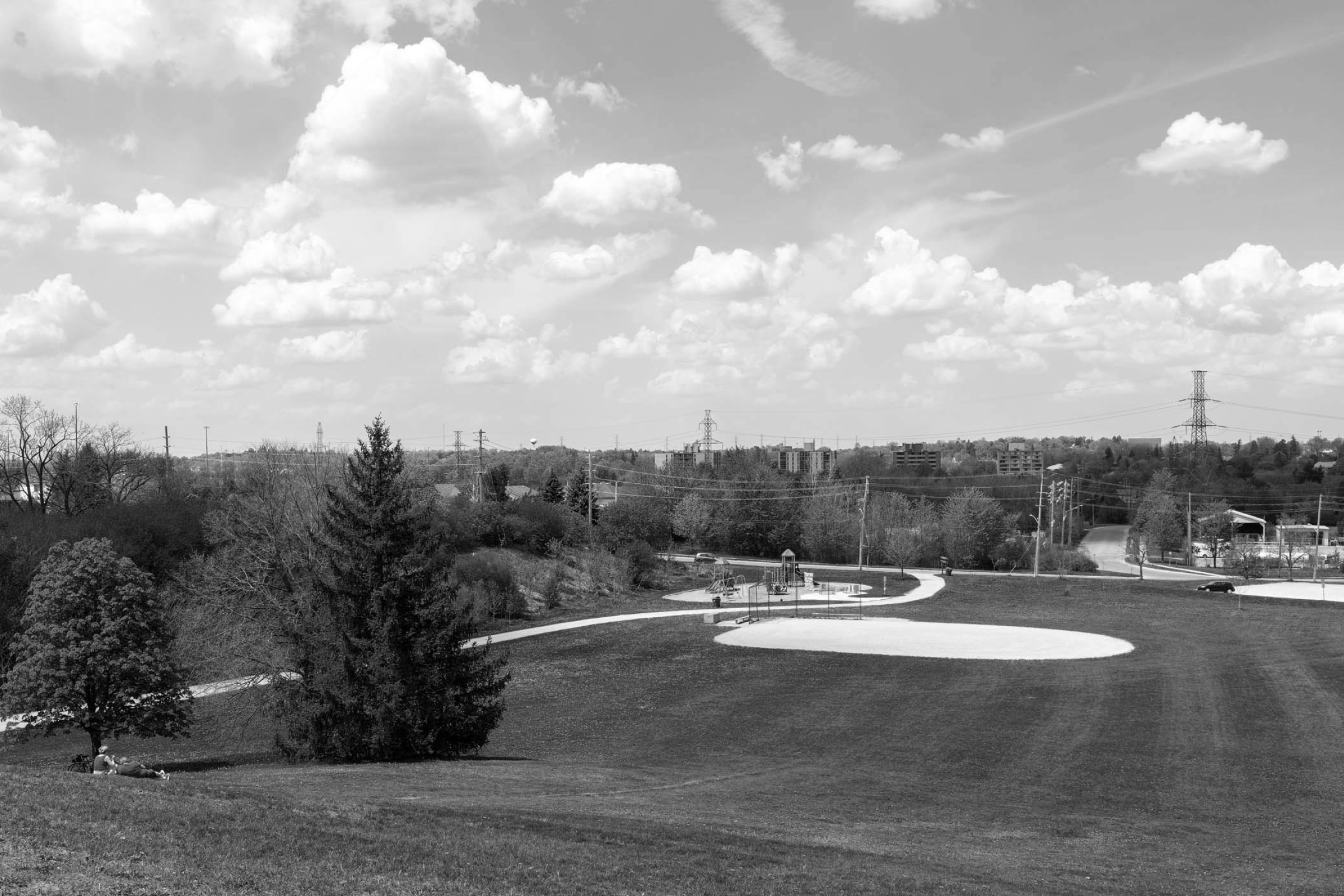 a photo of a baseball diamond and playground off in the distance, photo taken at the top of a hill and there are clouds in the sky