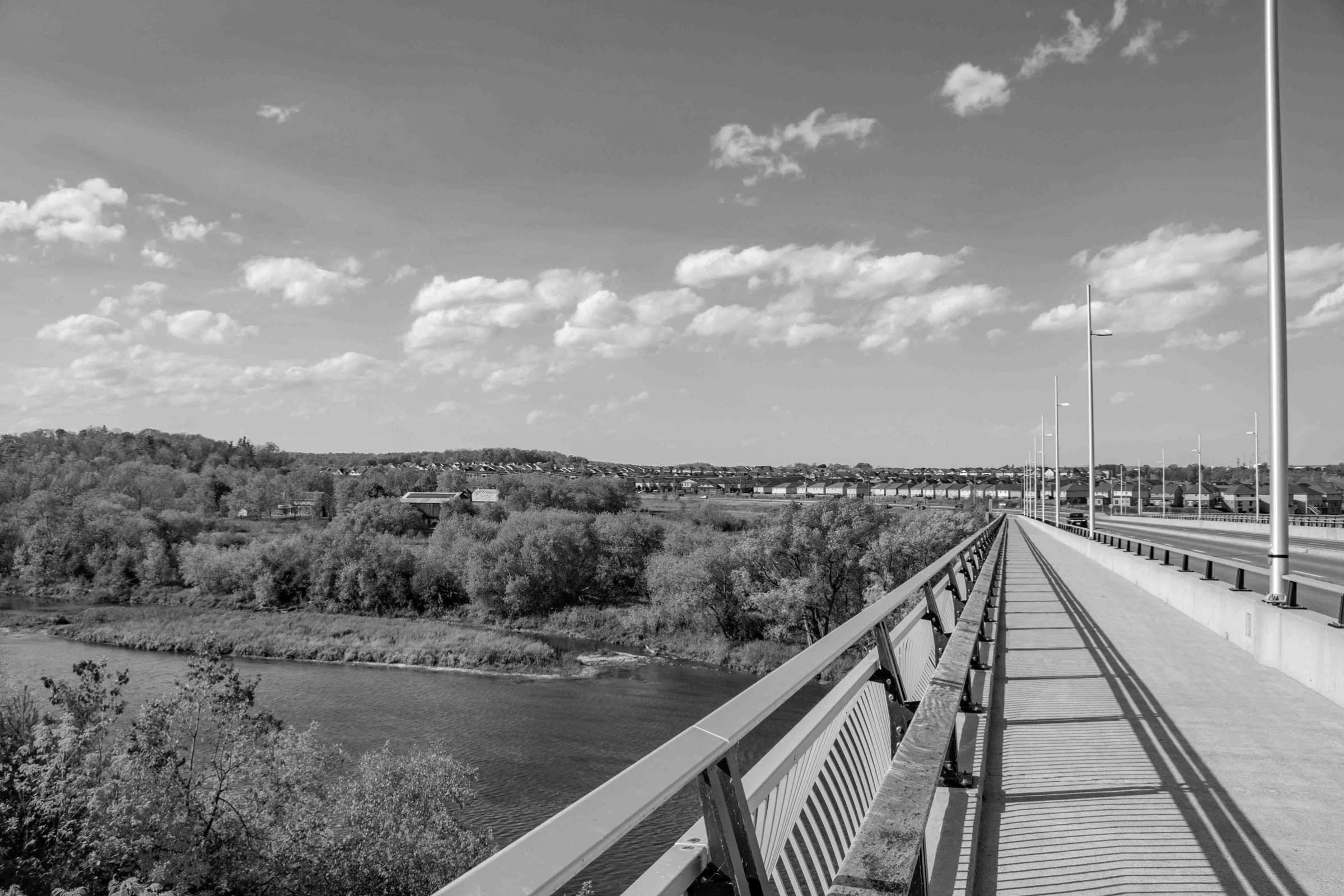 a photo overlooking the grand river from a pedestrian bridge over top and you can see the neighbourhood in the background and clouds in the sky